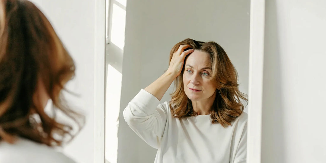 A woman gently checking her thinning hair crown in a mirror under soft natural light