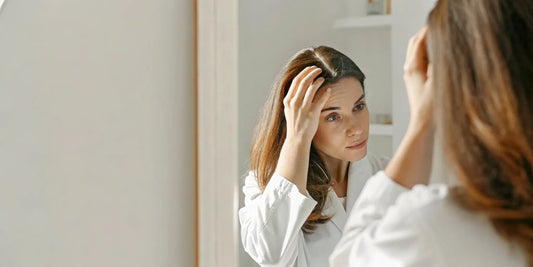 Woman looking in mirror, gently touching her hair, thoughtful expression, soft natural light